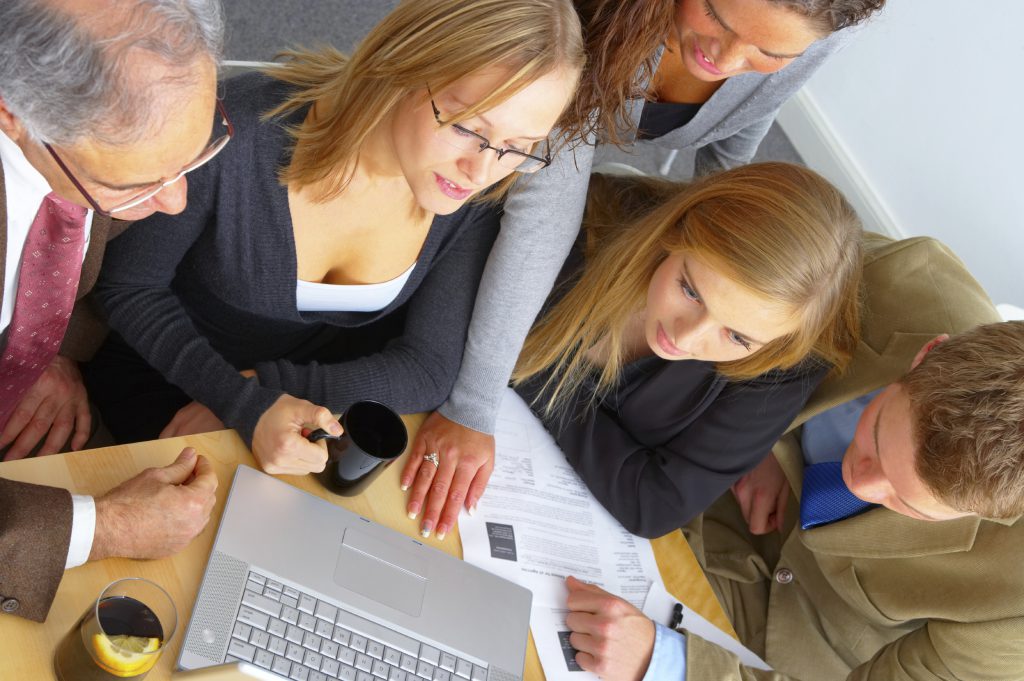Ein Team an Mitarbeiterinnen einer Firma im Gespräch an einem Tisch, mit Laptop und Materialien.