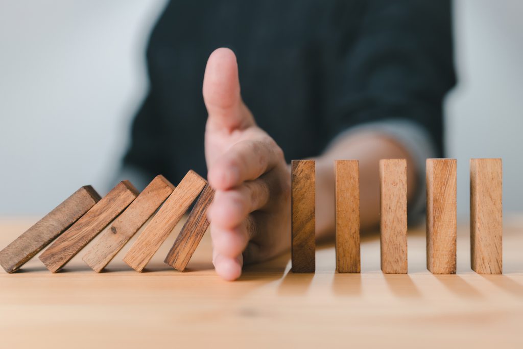 Dominosteine die aufgebaut sind, ein Teil ist umgefallen, ein Teil steht, dazwischen ist die Hand einer Person, steht symbolisch für Konfliktlösung.
